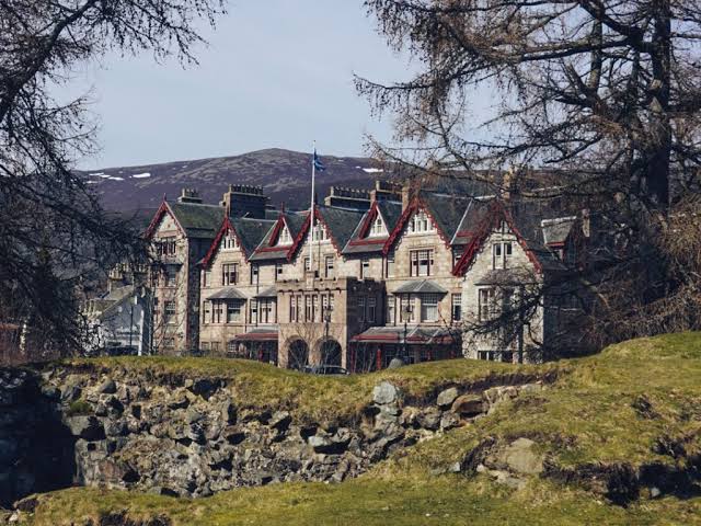 Stone hotel with red-trimmed gables below the hills in Braemar, Scotland