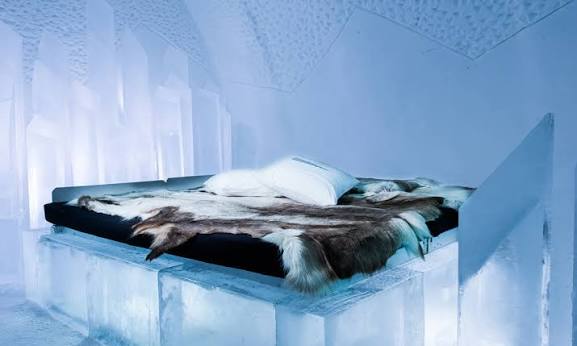 Ice-block bed with hides in a blue-lit room at Icehotel, Jukkasjarvi, Sweden